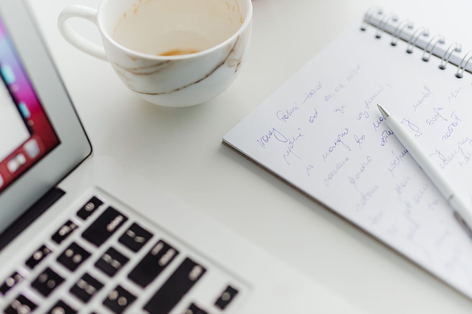 A cozy, modern workspace setup with a cup, laptop, and notes on a notebook.