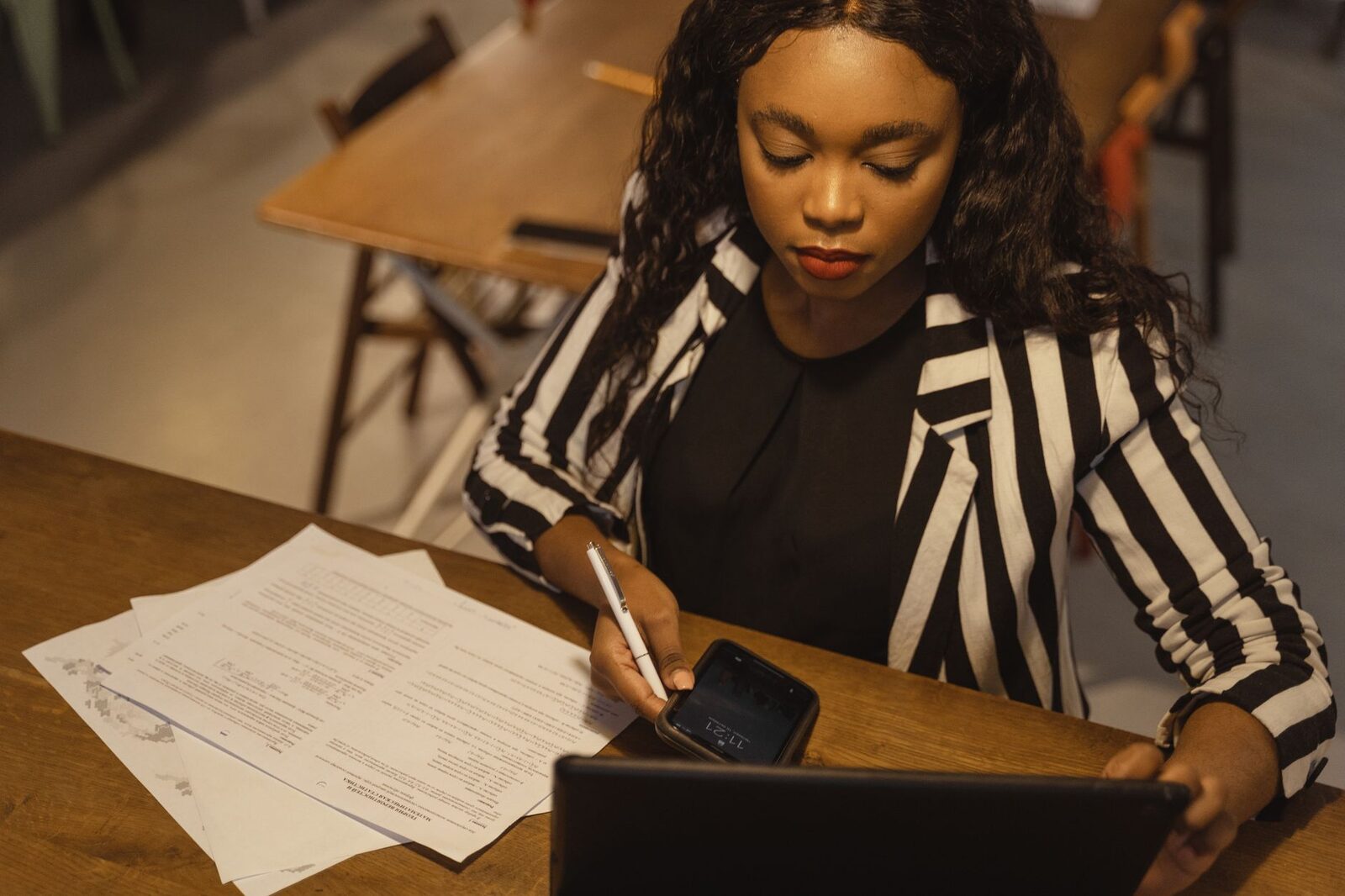 Focused woman in business attire working on a laptop with paperwork at a desk.